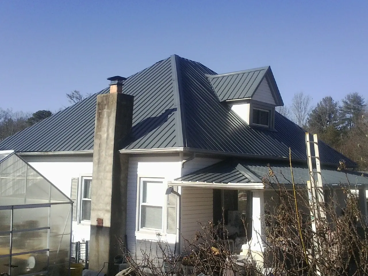 Dark blue standing seam metal roof on a white farmhouse with dormer — Slate & Tile Roof Repair by Roofing Brothers in Flom