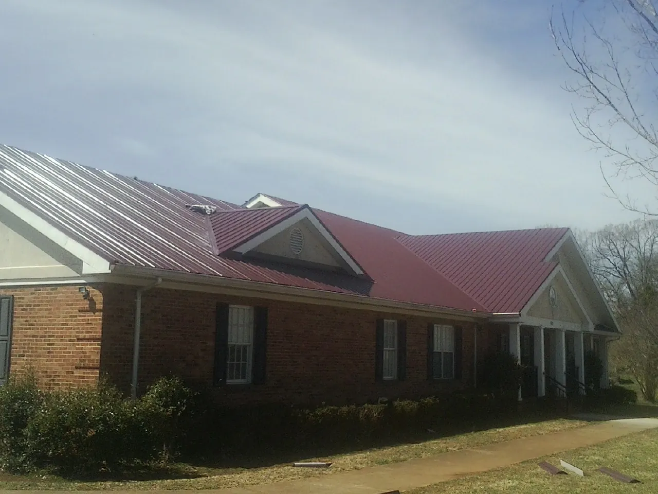 Red metal roof with gabled entries on a long brick building, from a Hail Damage Roof Repair job in Flom