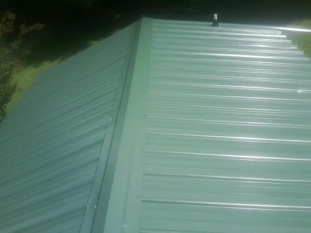 New green metal panels meeting at the ridge of a roof — Flat Roof Repair work by our crew in Flom