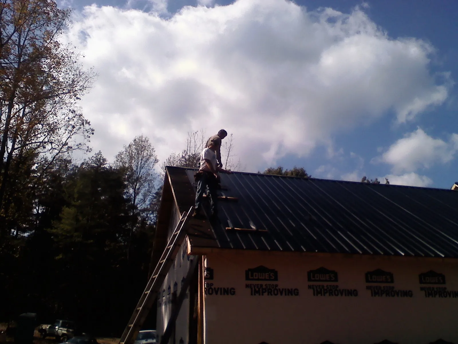 Roofer fastening dark metal panels high against a cloudy sky, from a Roof Inspection job in Flom
