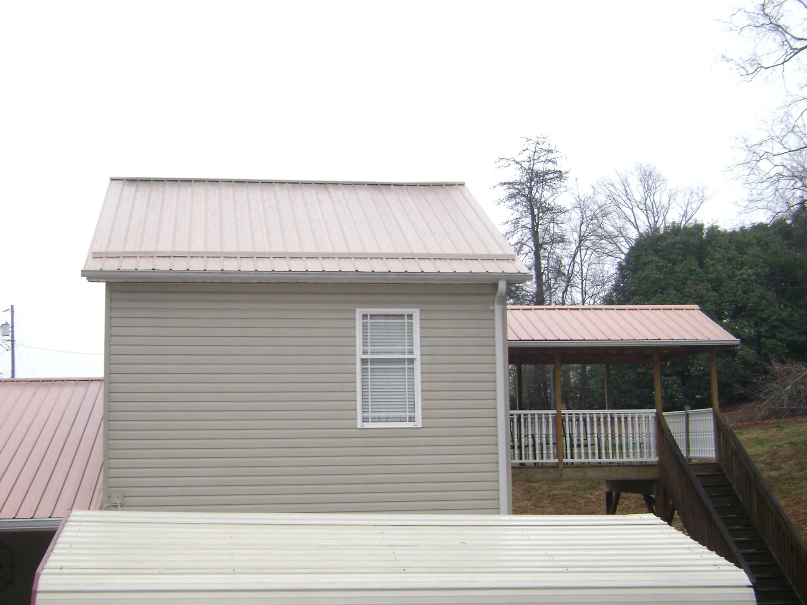 Tan metal roofs on a two story addition and attached porch, from a Roof Replacement job in Flom